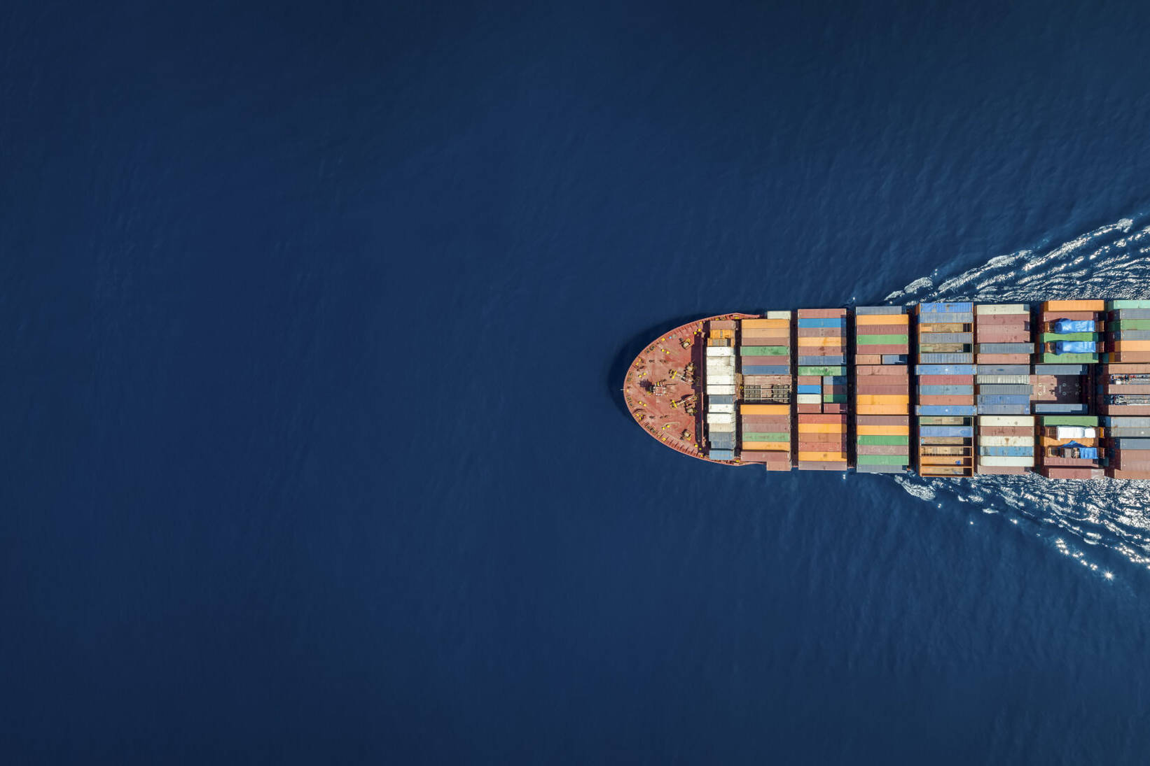 Aerial top down view of a large container cargo ship in motion over open ocean with copy space