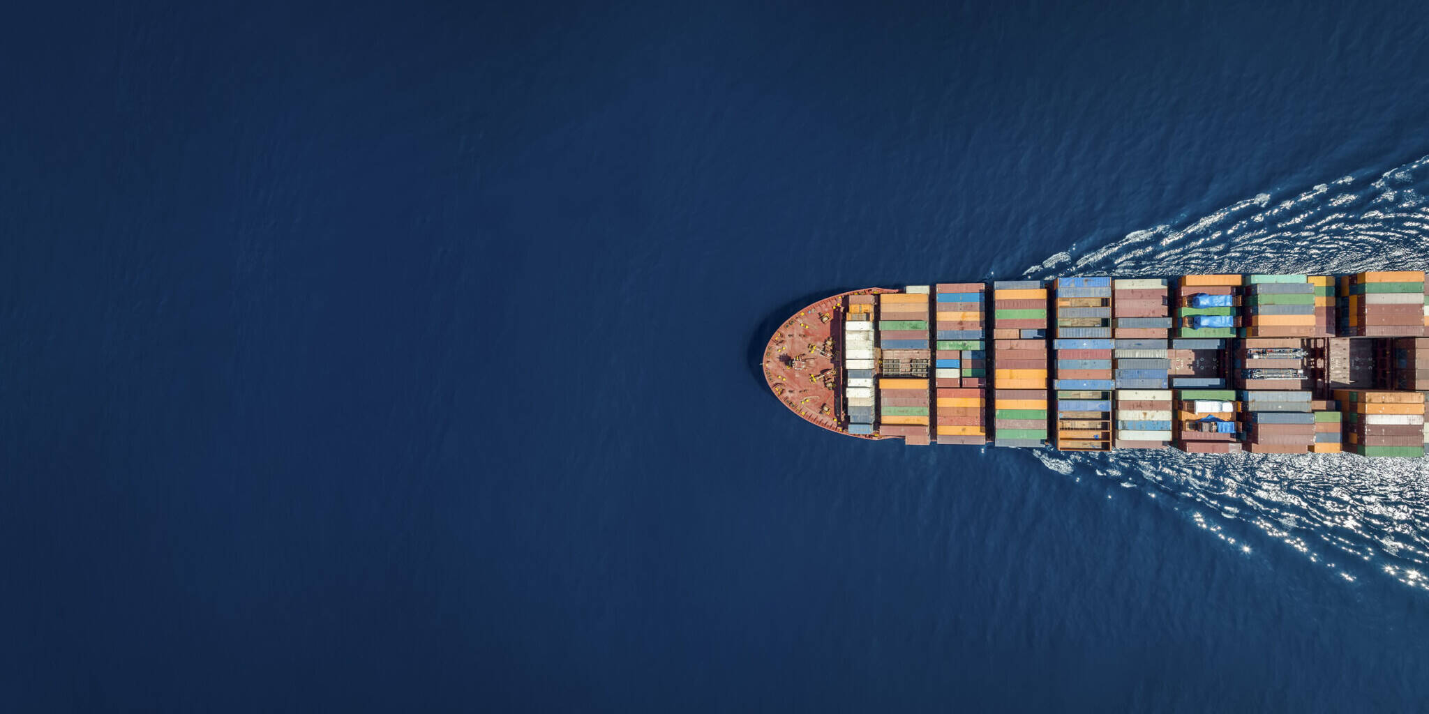 Aerial top down view of a large container cargo ship in motion over open ocean with copy space