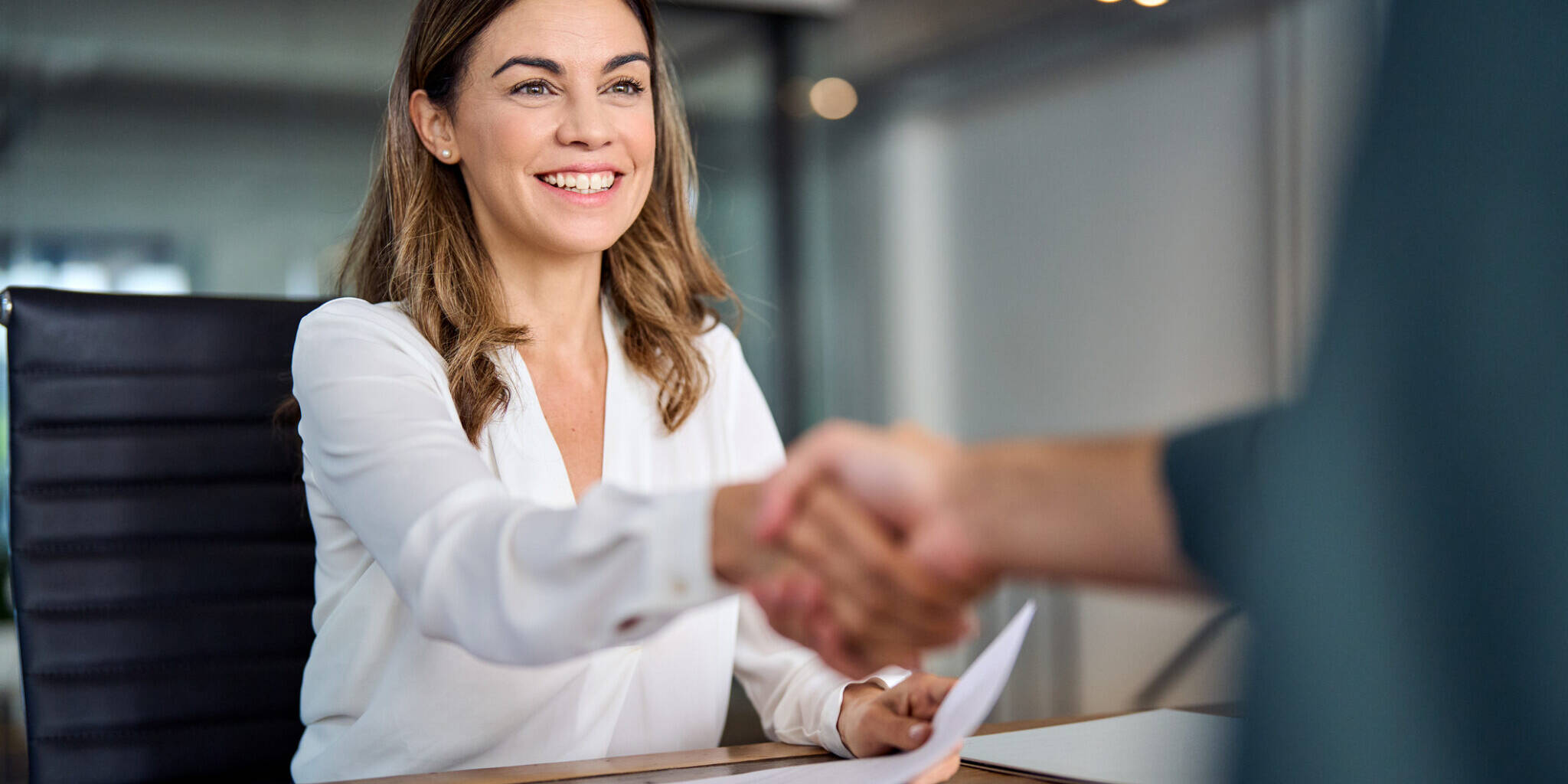 Happy mid aged business woman manager handshaking at office meeting. Smiling female hr hiring recruit at job interview, bank or insurance agent, lawyer making contract deal with client at work.